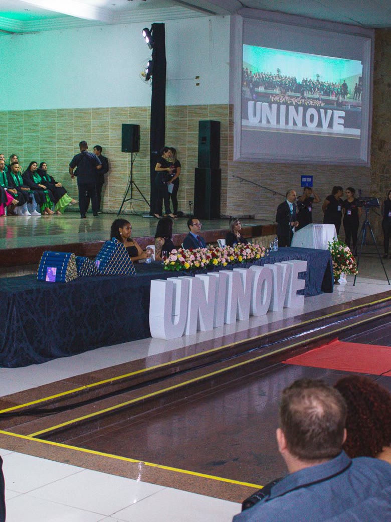 Solenidade de colação de grau com identidade visual UNINOVE, telão de transmissão e formandos no palco