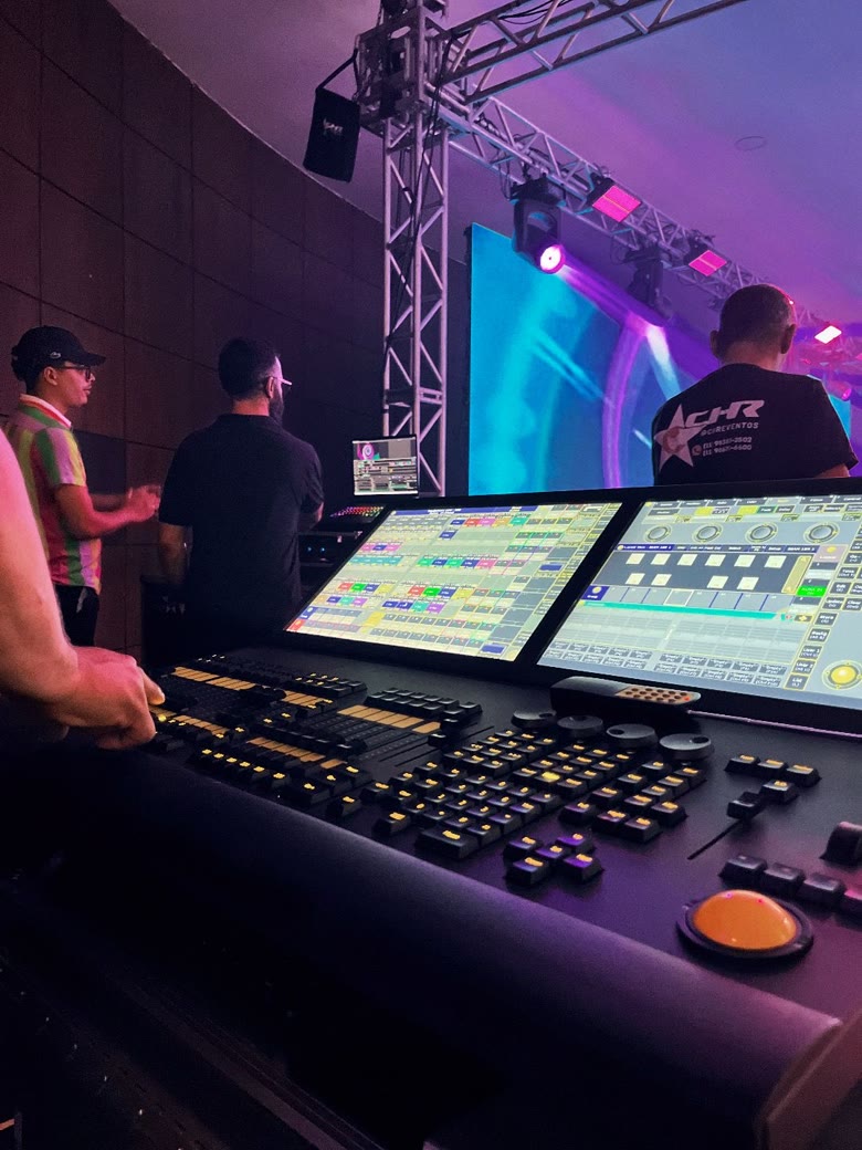 Mesa de controle de iluminação operada nos bastidores, com telão de LED ao fundo