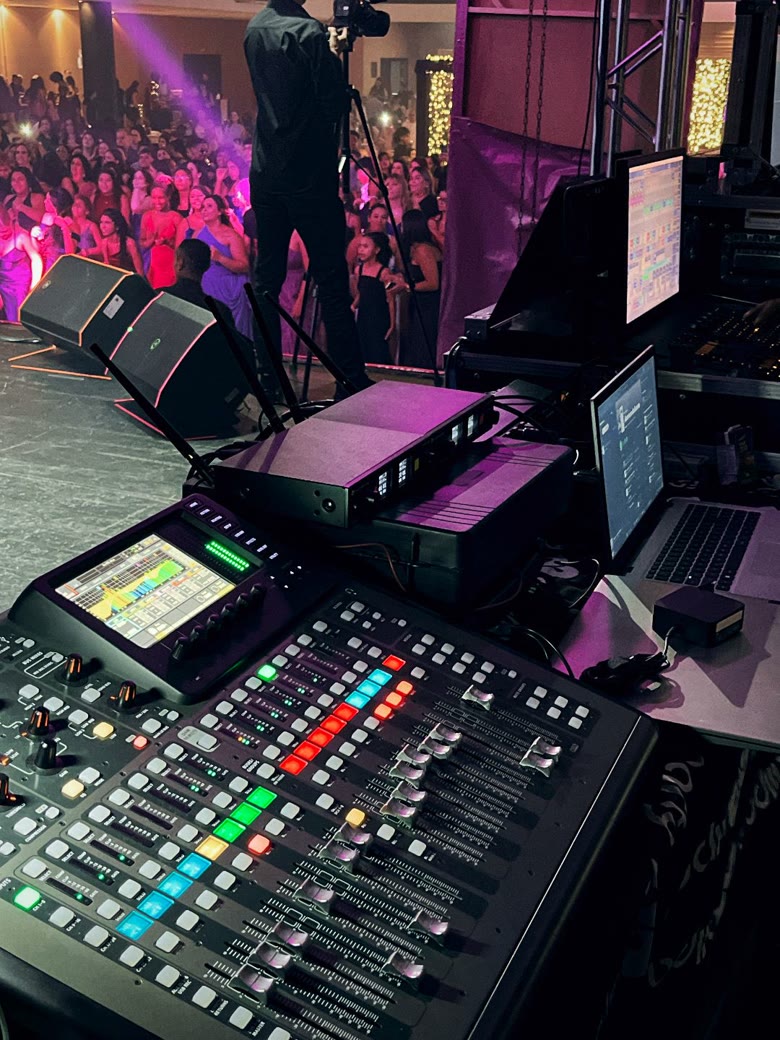 Mesa de mixagem digital em operação durante show, com pista lotada ao fundo