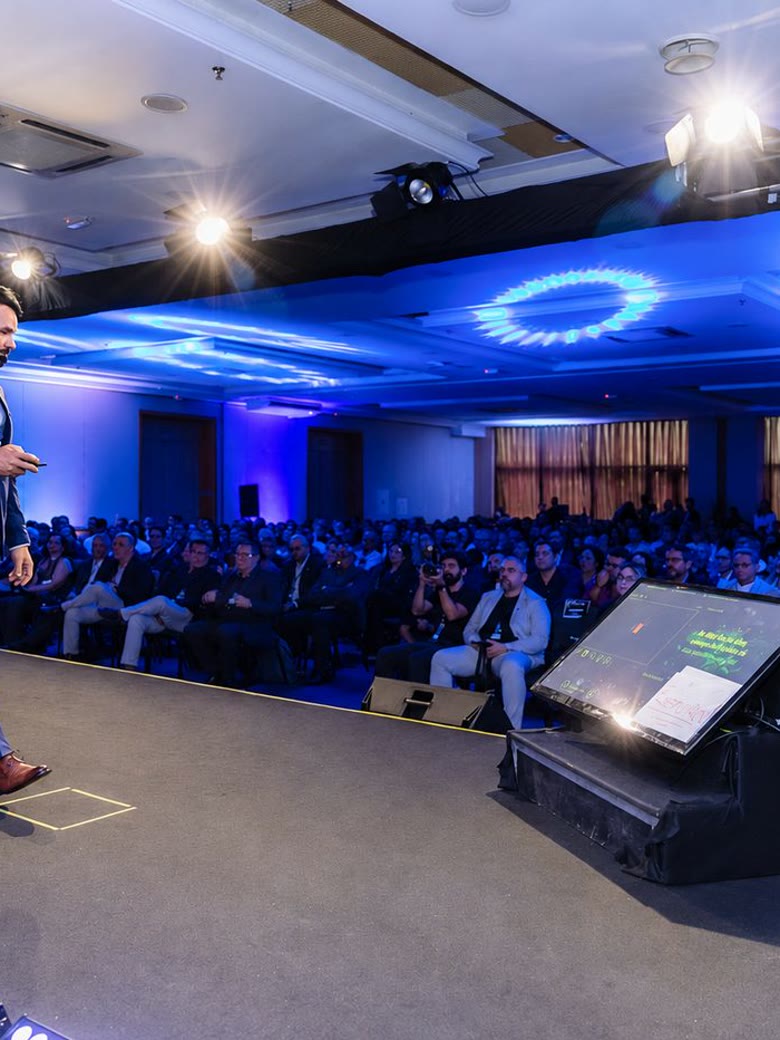Palestrante caminhando pelo palco durante keynote corporativo, com plateia e telão de LED