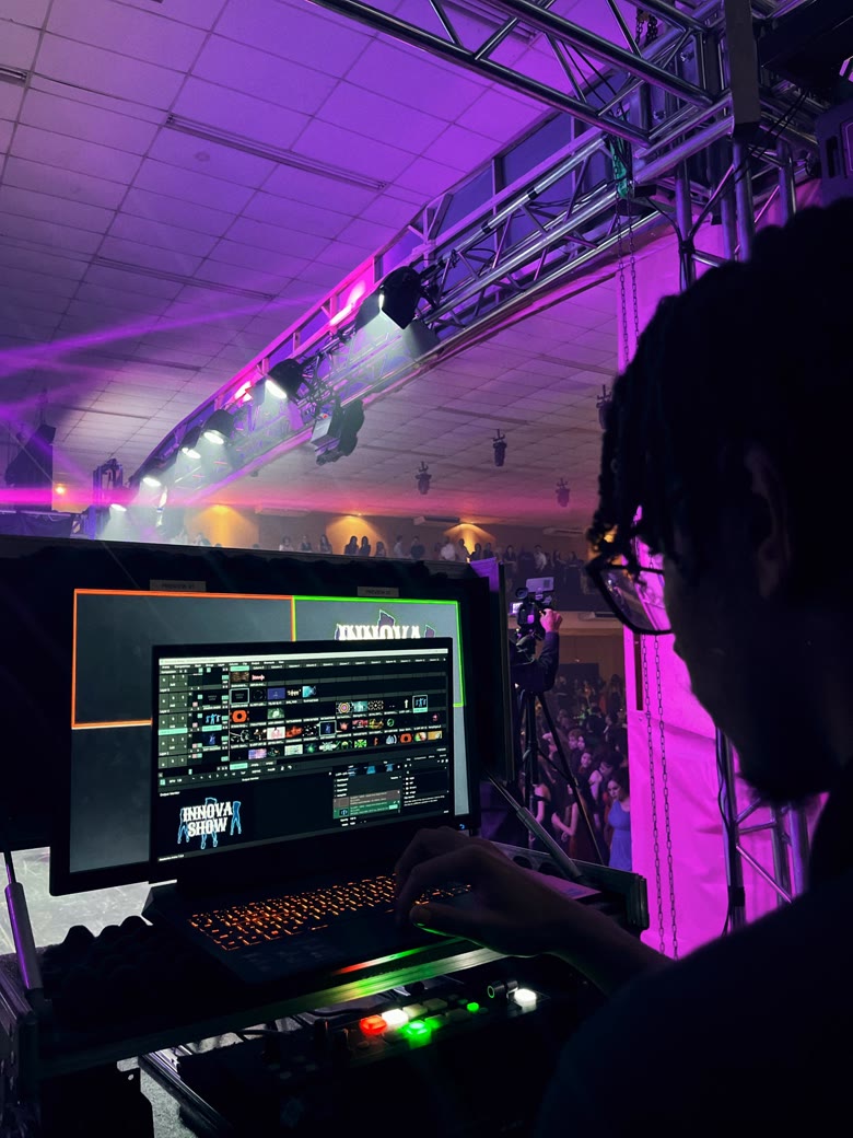 Operador de VJ sincronizando efeitos visuais do Innova Show ao vivo, com treliça de iluminação e multidão ao fundo